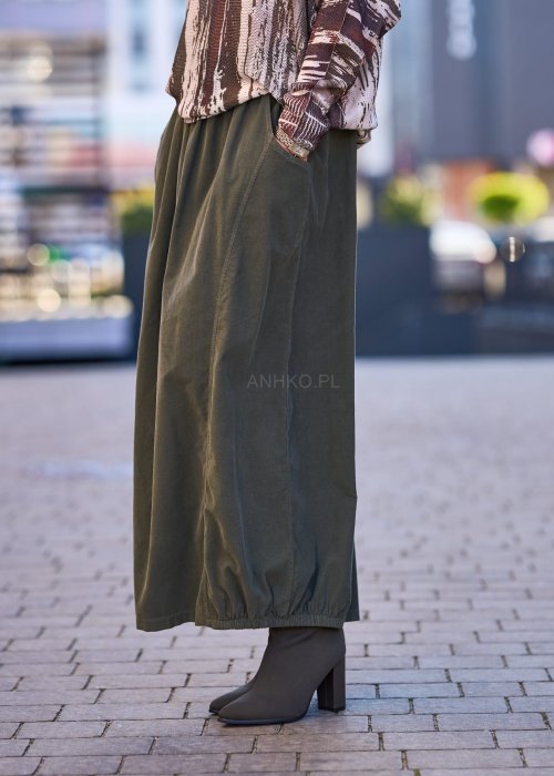 Spódnica maxi w kolorze khaki z elastyczną talią i kieszeniami, o luźnym kroju, zestawiona z wzorzystą bluzką i botkami na słupku w miejskiej stylizacji.