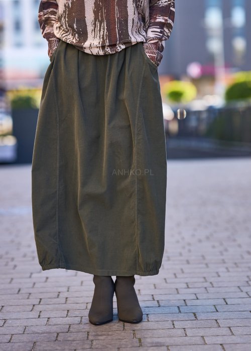 Spódnica maxi w kolorze khaki z elastyczną talią i kieszeniami, o luźnym kroju, zestawiona z wzorzystą bluzką i botkami na słupku w miejskiej stylizacji.