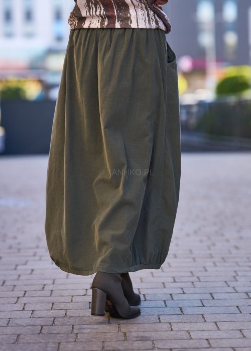 Spódnica maxi w kolorze khaki z elastyczną talią i kieszeniami, o luźnym kroju, zestawiona z wzorzystą bluzką i botkami na słupku w miejskiej stylizacji.