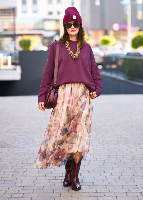 Śliwkowa bluza damska oversize z długim rękawem i naszywką, zestawiona ze wzorzystą spódnicą w stylizacji miejskiej.