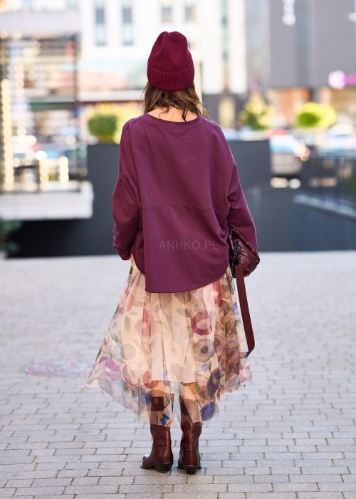 Śliwkowa bluza damska oversize z długim rękawem i naszywką, zestawiona ze wzorzystą spódnicą w stylizacji miejskiej.