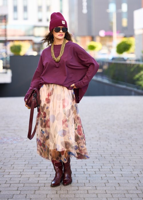 Śliwkowa bluza damska oversize z długim rękawem i naszywką, zestawiona ze wzorzystą spódnicą w stylizacji miejskiej.