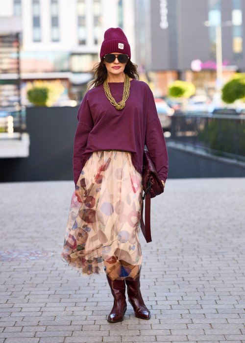 Śliwkowa bluza damska oversize z długim rękawem i naszywką, zestawiona ze wzorzystą spódnicą w stylizacji miejskiej.