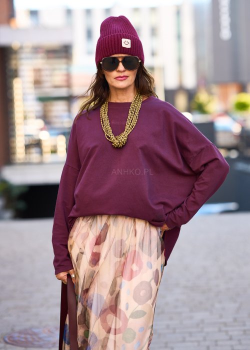 Śliwkowa bluza damska oversize z długim rękawem i naszywką, zestawiona ze wzorzystą spódnicą w stylizacji miejskiej.