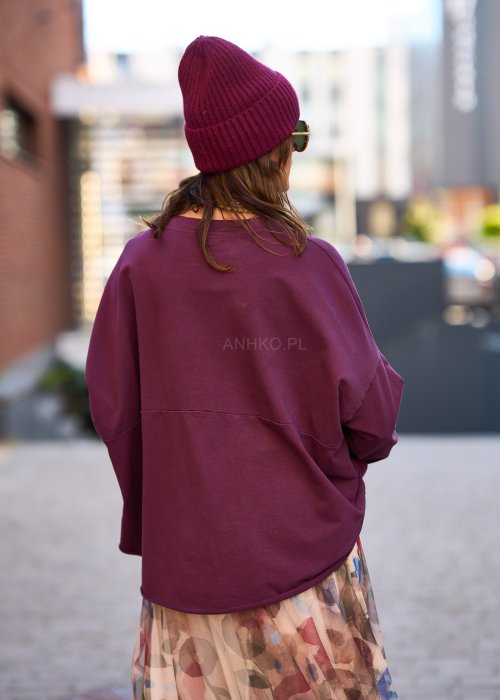 Śliwkowa bluza damska oversize z długim rękawem i naszywką, zestawiona ze wzorzystą spódnicą w stylizacji miejskiej.