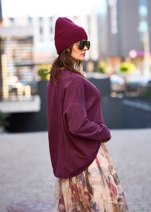 Śliwkowa bluza damska oversize z długim rękawem i naszywką, zestawiona ze wzorzystą spódnicą w stylizacji miejskiej.