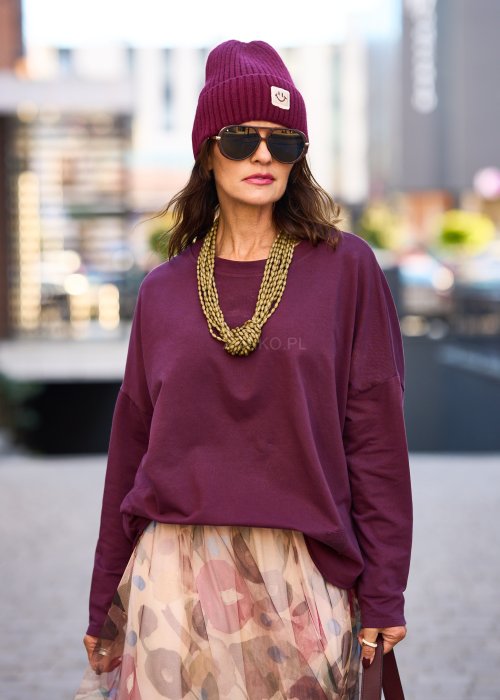 Śliwkowa bluza damska oversize z długim rękawem i naszywką, zestawiona ze wzorzystą spódnicą w stylizacji miejskiej.