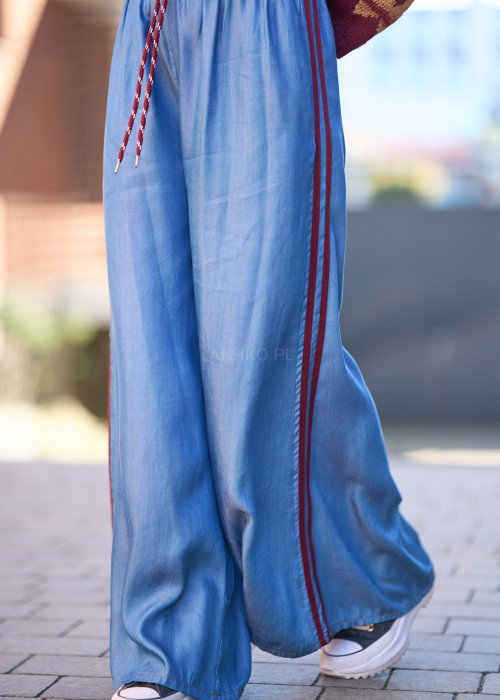 Niebieskie spodnie z lekkiego denimu o szerokich nogawkach, elastycznym pasie i ozdobnych lampasach w kolorze bordo