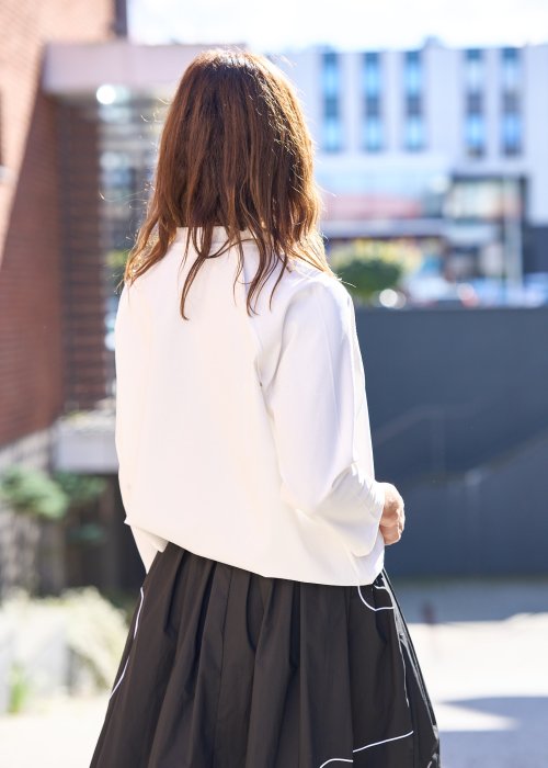 Biała bluzka koszulowa damska z dekoltem V i długim rękawem, o luźnym kroju. Stylizacja z czarną spódnicą w eleganckim, miejskim wydaniu.