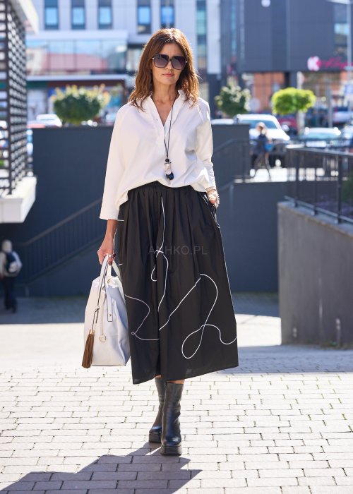 Biała bluzka koszulowa damska z dekoltem V i długim rękawem, o luźnym kroju. Stylizacja z czarną spódnicą w eleganckim, miejskim wydaniu.