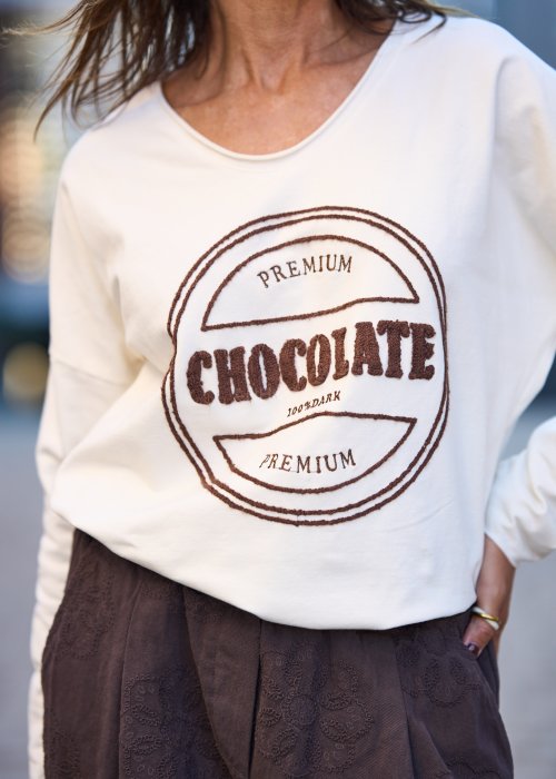 Biała bluzka damska Premium Chocolate z haftowanym napisem na przodzie, dekoltem w serek i luźnym fasonem do codziennych stylizacji.