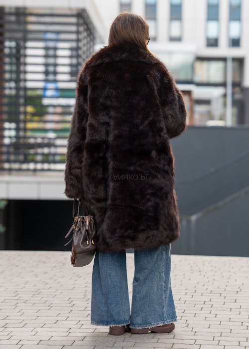 Długi brązowy płaszcz futrzany Kavara o luźnym fasonie oversize i dużym wykładanym kołnierzu, zestawiony z jeansami wide leg.
