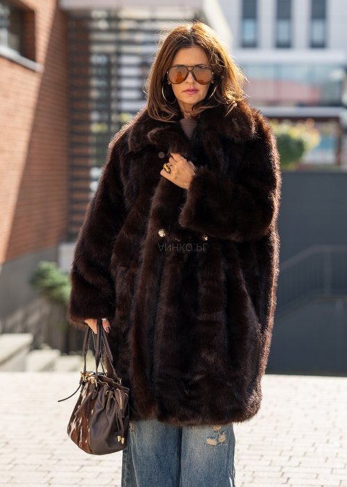 Długi brązowy płaszcz futrzany Kavara o luźnym fasonie oversize i dużym wykładanym kołnierzu, zestawiony z jeansami wide leg.
