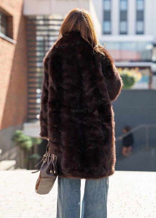 Długi brązowy płaszcz futrzany Kavara o luźnym fasonie oversize i dużym wykładanym kołnierzu, zestawiony z jeansami wide leg.