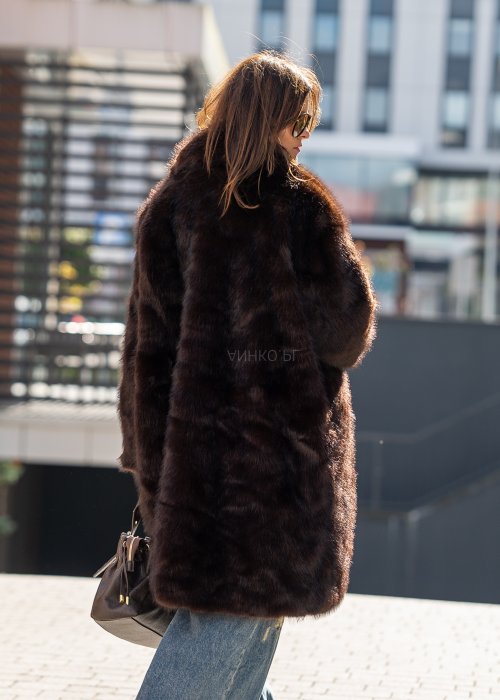 Długi brązowy płaszcz futrzany Kavara o luźnym fasonie oversize i dużym wykładanym kołnierzu, zestawiony z jeansami wide leg.