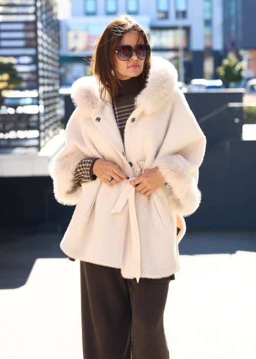 Krótka kurtka typu ponczo w kolorze ecru z kapturem i futrzanym wykończeniem rękawów