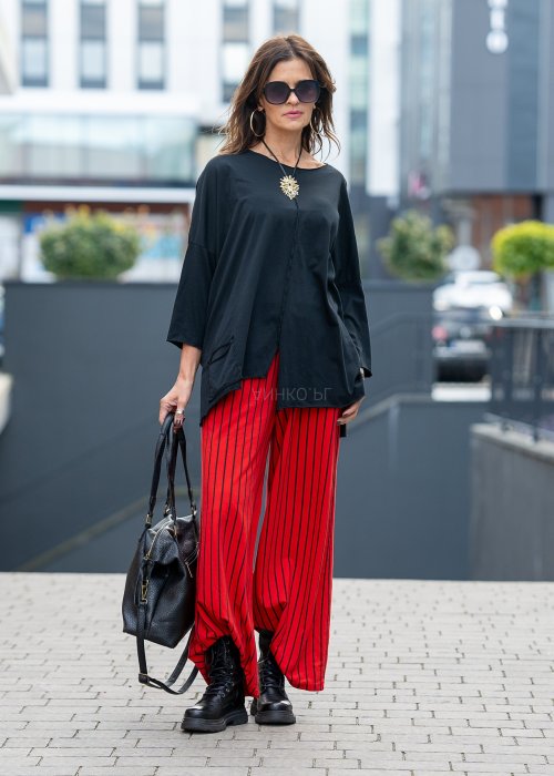 Czerwone spodnie damskie w czarne pionowe paski o szerokim kroju, zestawione z czarną bluzą i botkami na obcasie w nowoczesnej stylizacji.