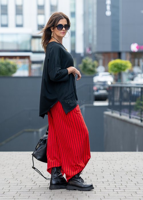 Czerwone spodnie damskie w czarne pionowe paski o szerokim kroju, zestawione z czarną bluzą i botkami na obcasie w nowoczesnej stylizacji.