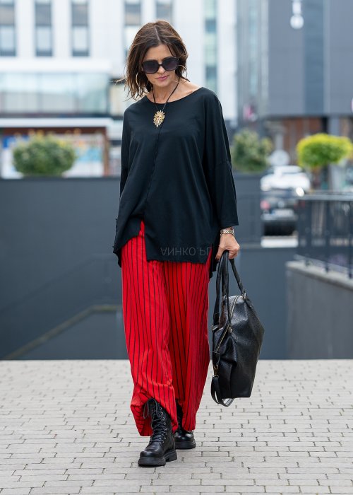 Czerwone spodnie damskie w czarne pionowe paski o szerokim kroju, zestawione z czarną bluzą i botkami na obcasie w nowoczesnej stylizacji.