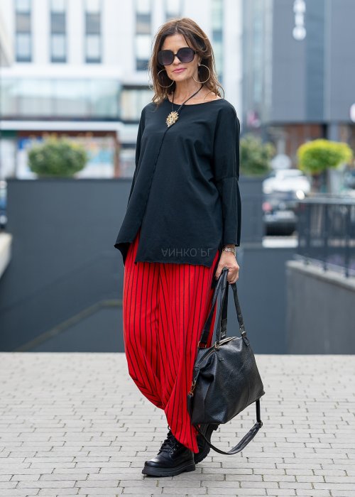 Czerwone spodnie damskie w czarne pionowe paski o szerokim kroju, zestawione z czarną bluzą i botkami na obcasie w nowoczesnej stylizacji.