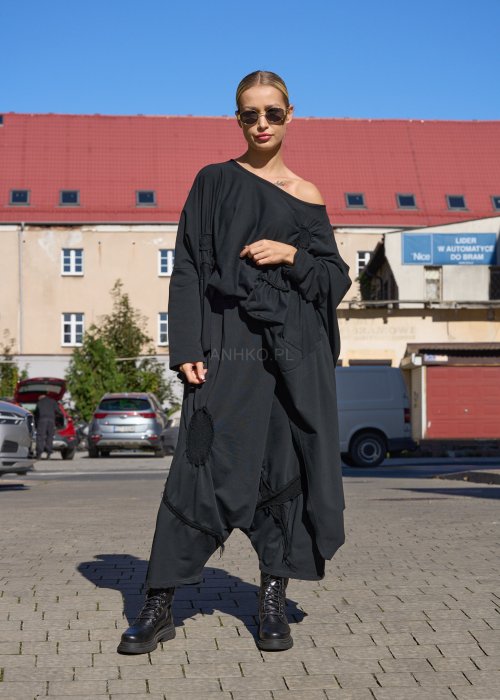 Czarne spodnie damskie oversize z obniżonym krokiem i ozdobnymi aplikacjami, zestawione z botkami i luźną bluzą w nowoczesnej stylizacji streetwear.