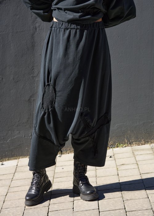 Czarne spodnie damskie oversize z obniżonym krokiem i ozdobnymi aplikacjami, zestawione z botkami i luźną bluzą w nowoczesnej stylizacji streetwear.