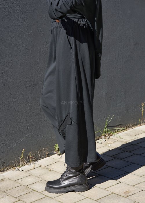 Czarne spodnie damskie oversize z obniżonym krokiem i ozdobnymi aplikacjami, zestawione z botkami i luźną bluzą w nowoczesnej stylizacji streetwear.