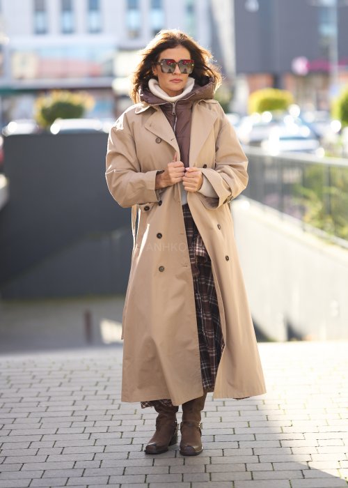 Długi beżowy trencz damski z paskiem w talii, dwurzędowe guziki, klasyczny fason