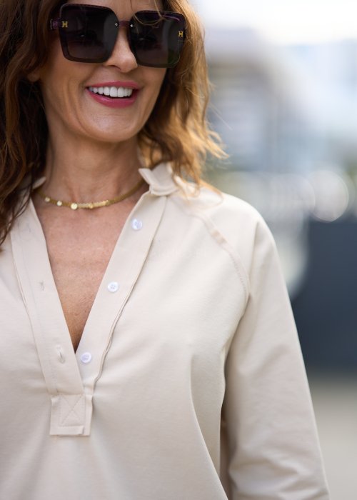 Beżowa koszula damska z długim rękawem i dekoltem zapinanym na guziki, wykonana z lekkiej tkaniny o luźnym kroju