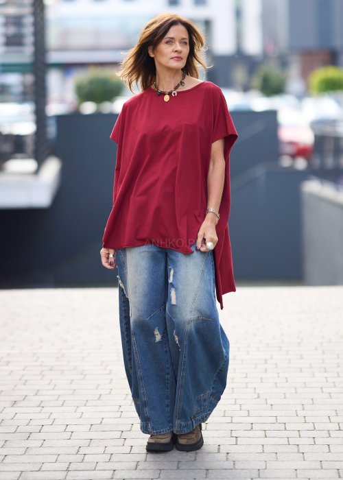 Bordowa bluzka oversize z asymetrycznym dołem i wydłużonym tyłem, zestawiona z jasnymi jeansami. Luźny fason i gładki materiał nadają stylizacji nowoczesny, miejski charakter.