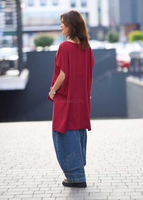 Bordowa bluzka oversize z asymetrycznym dołem i wydłużonym tyłem, zestawiona z jasnymi jeansami. Luźny fason i gładki materiał nadają stylizacji nowoczesny, miejski charakter.