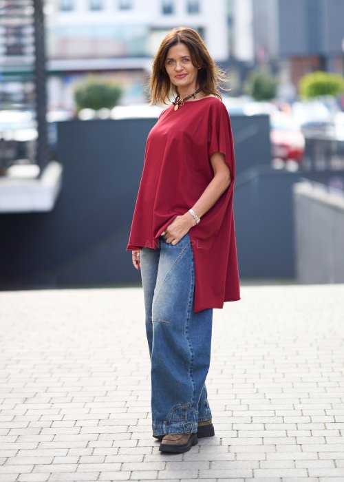 Bordowa bluzka oversize z asymetrycznym dołem i wydłużonym tyłem, zestawiona z jasnymi jeansami. Luźny fason i gładki materiał nadają stylizacji nowoczesny, miejski charakter.