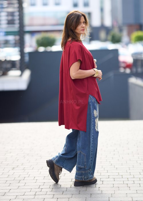 Bordowa bluzka oversize z asymetrycznym dołem i wydłużonym tyłem, zestawiona z jasnymi jeansami. Luźny fason i gładki materiał nadają stylizacji nowoczesny, miejski charakter.