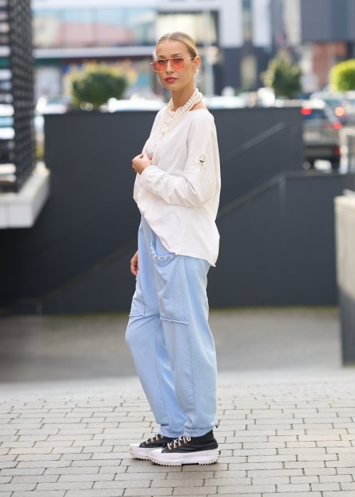 Jasnoniebieskie spodnie harem damskie z dużymi kieszeniami ozdobionymi perłami i elastyczną talią, stylizowane w miejskim looku ze sneakersami.