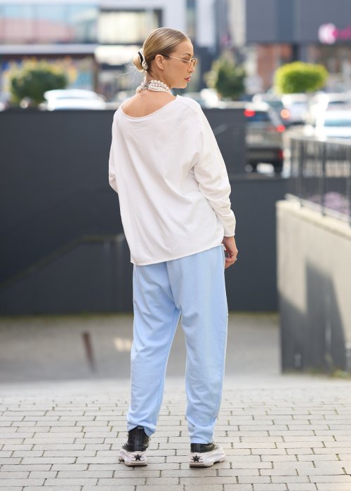 Jasnoniebieskie spodnie harem damskie z dużymi kieszeniami ozdobionymi perłami i elastyczną talią, stylizowane w miejskim looku ze sneakersami.