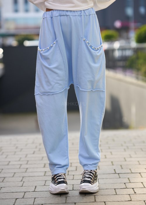 Jasnoniebieskie spodnie harem damskie z dużymi kieszeniami ozdobionymi perłami i elastyczną talią, stylizowane w miejskim looku ze sneakersami.