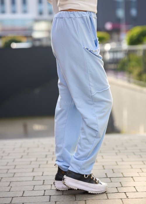 Jasnoniebieskie spodnie harem damskie z dużymi kieszeniami ozdobionymi perłami i elastyczną talią, stylizowane w miejskim looku ze sneakersami.