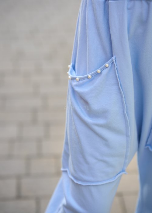 Jasnoniebieskie spodnie harem damskie z dużymi kieszeniami ozdobionymi perłami i elastyczną talią, stylizowane w miejskim looku ze sneakersami.