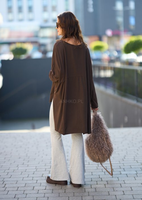 Czekoladowa bluzka oversize z dłuższym tyłem i długim rękawem, zestawiona z niebieskimi jeansami w swobodnej, miejskiej stylizacji.