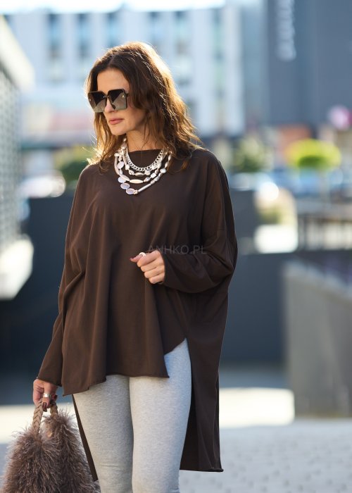 Czekoladowa bluzka oversize z dłuższym tyłem i długim rękawem, zestawiona z niebieskimi jeansami w swobodnej, miejskiej stylizacji.