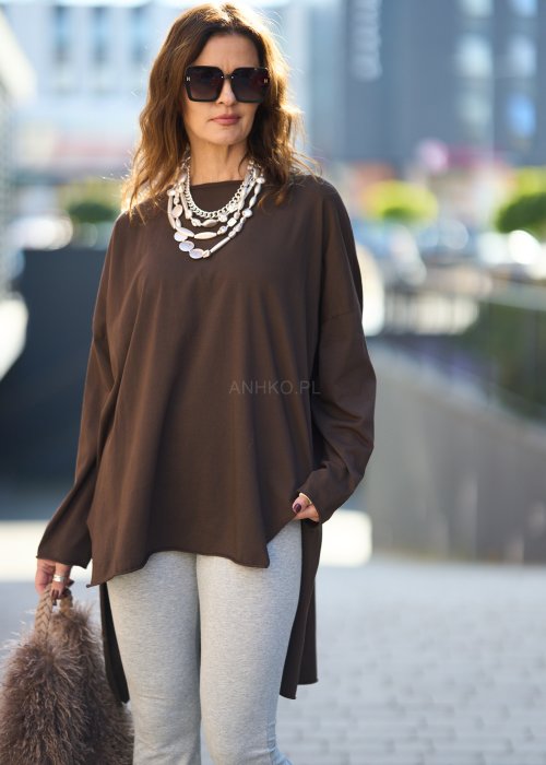 Czekoladowa bluzka oversize z dłuższym tyłem i długim rękawem, zestawiona z niebieskimi jeansami w swobodnej, miejskiej stylizacji.
