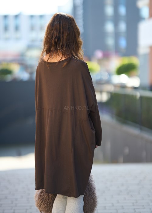 Czekoladowa bluzka oversize z dłuższym tyłem i długim rękawem, zestawiona z niebieskimi jeansami w swobodnej, miejskiej stylizacji.