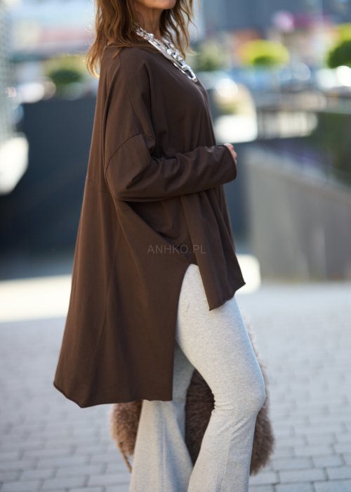 Czekoladowa bluzka oversize z dłuższym tyłem i długim rękawem, zestawiona z niebieskimi jeansami w swobodnej, miejskiej stylizacji.