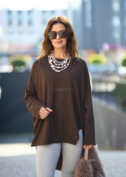 Czekoladowa bluzka oversize z dłuższym tyłem i długim rękawem, zestawiona z niebieskimi jeansami w swobodnej, miejskiej stylizacji.