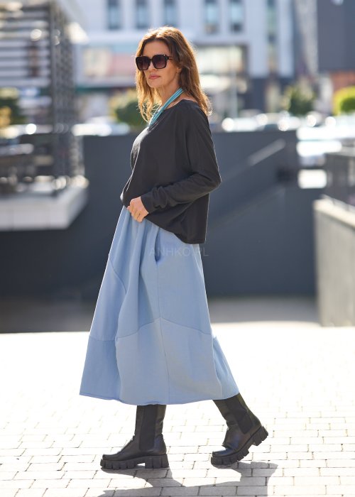 Czarna bluzka oversize z długim rękawem i szerokim dekoltem, zestawiona z jasnoniebieską spódnicą w nowoczesnej, miejskiej stylizacji.