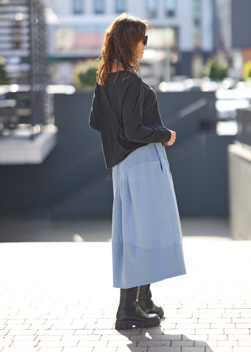 Czarna bluzka oversize z długim rękawem i szerokim dekoltem, zestawiona z jasnoniebieską spódnicą w nowoczesnej, miejskiej stylizacji.