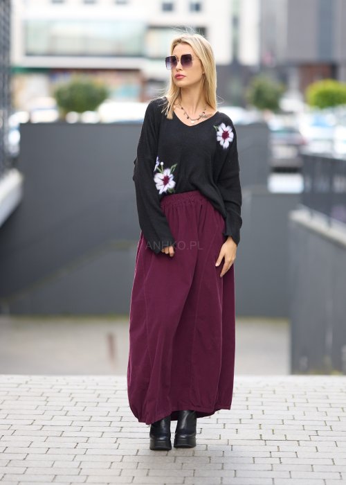 Śliwkowa spódnica maxi z elastyczną talią i kieszeniami, o luźnym kroju, zestawiona z czarną bluzą i czarnymi botkami na obcasie w miejskiej stylizacji.