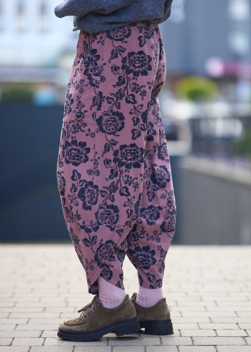 Różowe spodnie damskie z luźną nogawką i czarnym kwiatowym wzorem, wykonane z lekkiego materiału z kieszeniami