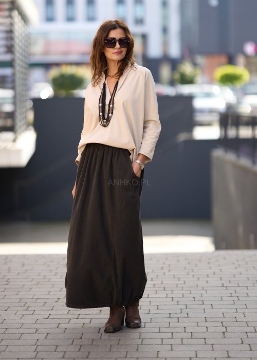 Brązowa spódnica maxi z elastyczną talią i kieszeniami, o luźnym kroju, zestawiona z beżową bluzką i brązowymi botkami w eleganckiej, miejskiej stylizacji.