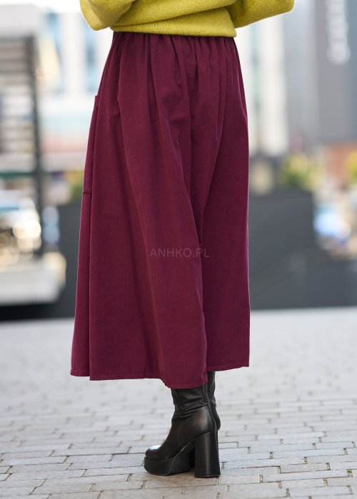 Śliwkowa spódnica sztruksowa midi z naszywanymi kieszeniami i elastycznym pasem, zestawiona z limonkowym swetrem i czarnymi botkami w miejskiej stylizacji.